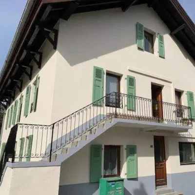 a white building with green shutters and a balcony at Appartement Chamonix Bossons in Chamonix-Mont-Blanc