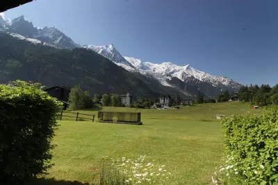 a field with a bench and mountains in the background at Le Savoy - Terrasse avec vue sur le Mont-Blanc in Chamonix-Mont-Blanc