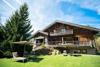 a large log house with chairs and an umbrella at Chalet Mozart I Le Chalet Club in Megève