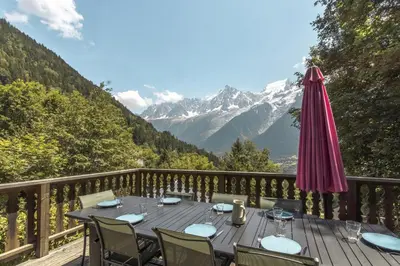 a table with chairs and an umbrella on a balcony with mountains at Datcha of Sky -Jardin - Calme - 180 vues - 9 chambres & Studio Appt in Les Houches