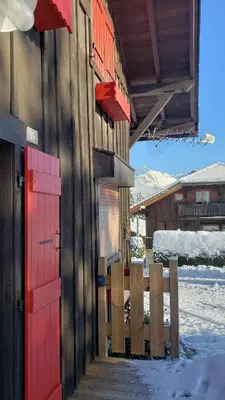 a building with red doors and a fence in the snow at Le Mazot de Janton in Combloux