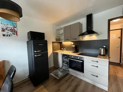 a kitchen with a black refrigerator and white cabinets at Cosy Criou - Appartement avec vue sur la montagne in Samoëns