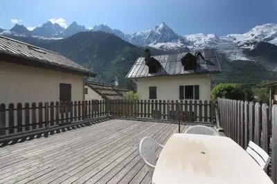 a wooden deck with a table and chairs and mountains at L'Ecrin des Pècles - Centrale - Rénové - Immense Terrasse Face au Mont-Blanc in Chamonix-Mont-Blanc