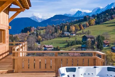 a hot tub on a deck with mountains in the background at Chalet vue Mont Blanc avec jacuzzi extérieur in Combloux