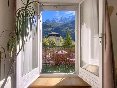 an open door to a balcony with a table and mountains at STUDIO LIMBO CHAMONIX HYPER CENTRE Vue imprenable sur le Mont-blanc in Chamonix-Mont-Blanc