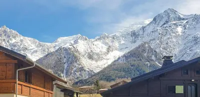 a snow covered mountain range with a house in the foreground at La Griaz - Chaleureux et cosy -Vue sur les montagnes - grand balcon in Les Houches