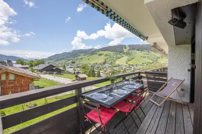 a dining table on a balcony with a view of the mountains at Les Corneilles - Appartement in Megève