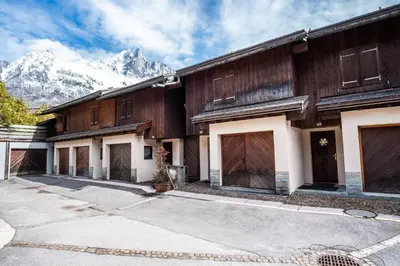 a house with wooden doors and mountains in the background at Clos des vorgeats 3 - Téléphérique, Terrain de Folf, Randonnée et Bus à la porte in Chamonix-Mont-Blanc