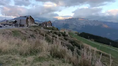 a building on a hill with a mountain in the background at Appartement pied des pistes - Samoëns 1600 in Samoëns
