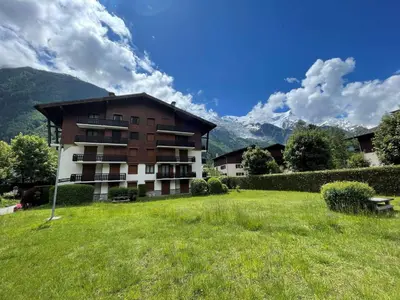 a large building in a field of grass with mountains at Appartement avec balcon, parking et animaux acceptés à Chamonix - FR-1-343-245 in Chamonix-Mont-Blanc