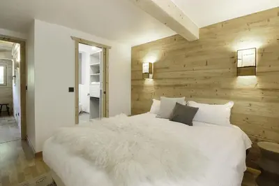 a bedroom with a white bed with a wooden wall at Chalet Béchar Le Magnifique- Garden - Sauna & Jacuzzi in Les Houches