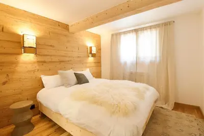 a bedroom with a white bed with a wooden wall at Chalet Béchar Le Magnifique- Garden - Sauna & Jacuzzi in Les Houches