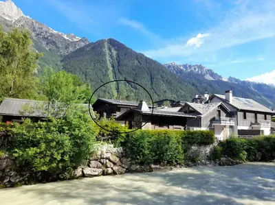 a house next to a river with mountains in the background at Chalet Claudia by Brennus Chamonix in Chamonix-Mont-Blanc