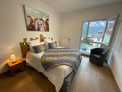 a bedroom with a bed and a chair and a window at Appartement au pied du Mont-Blanc 2! in Sallanches