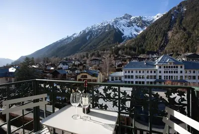 a table with wine glasses on a balcony with mountains at Majestic T2 calme, spacieux, central, avec parking in Chamonix-Mont-Blanc