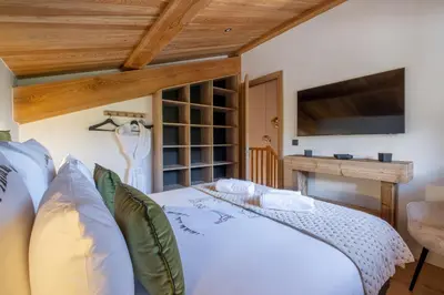 a bedroom with a white bed and a flat screen tv at Chalet Ango I Jacuzzi & Hammam I Proche télécabine in Combloux