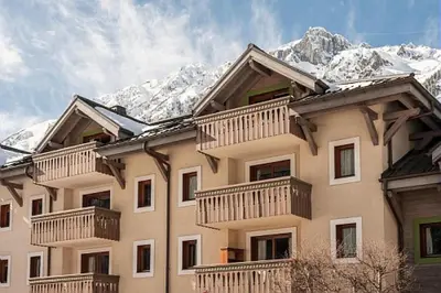 a large building with balconies and snow covered mountains at Résidence La Ginabelle - maeva Home - Appartement 3 pièces 6 personnes - Prestige MAE-4054 in Chamonix-Mont-Blanc