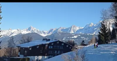 a house on a snowy hill with mountains in the background at Studio porte du Mont Blanc Combloux aux pieds des pistes in Combloux
