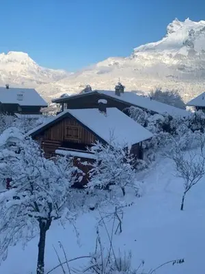 a house covered in snow with mountains in the background at Chalet le jardin de fées in Saint-Gervais-les-Bains