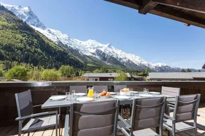 a table on a balcony with a view of mountains at Grand Paradis- Modern 3 bedroom apartment with spectacular views in Chamonix-Mont-Blanc