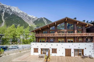 a large house with a wooden roof with mountains in the background at Grand Paradis- Modern 3 bedroom apartment with spectacular views in Chamonix-Mont-Blanc