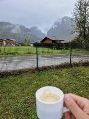 a person holding a cup of coffee in front of a fence at Charmant mobilhome à 2 pas remontés ski Samoëns in Samoëns
