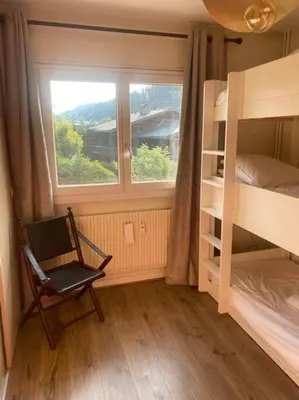 a bedroom with a window and a chair and bunk beds at Appartement Au pied du Jaillet in Megève