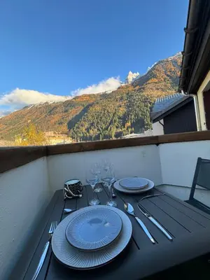 a table with plates and wine glasses on a balcony at Cocon au cœur de Chamonix avec parking gratuit in Chamonix-Mont-Blanc