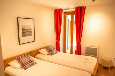 two beds in a room with red curtains and a window at 3 bed apt,central location, parking, garden, 6 pax in Saint-Gervais-les-Bains