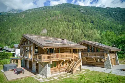 a large wooden house with a deck and mountains in the background at Chalets ASA 426 m2 in Chamonix-Mont-Blanc