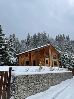 a wooden house with a stone wall in the snow at Chalet aux Cerfs - Maison pour 10 vue montagne in Arâches-la-Frasse