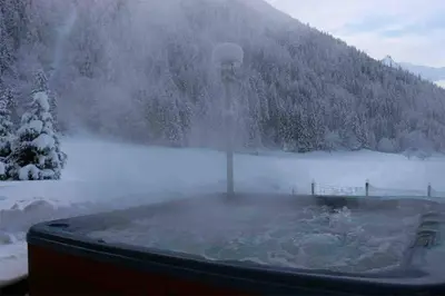 a hot tub in front of a snow covered lake at Chalet Melusine - Big Chalet w Spa Pool, Sauna, Huge Terrace, Views & Privacy! in Argentiere