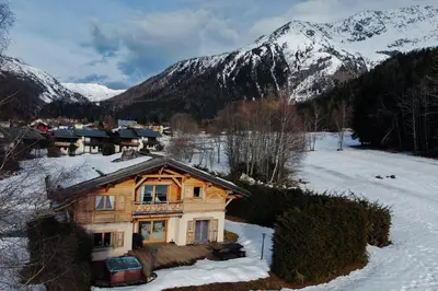 a wooden house in the snow with mountains in the background at Chalet Melusine - Big Chalet w Spa Pool, Sauna, Huge Terrace, Views & Privacy! in Argentiere