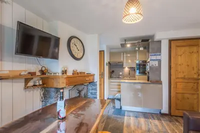 a living room with a clock on the wall and a kitchen at Appartement Sous-Bois - Welkeys in Chamonix-Mont-Blanc