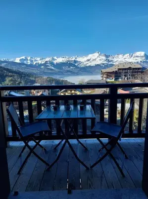 a table and chairs on a deck with snow covered mountains at Appartement Saint Gervais proche centre in Saint-Gervais-les-Bains