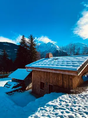 a building covered in snow with mountains in the background at Chalet du Bonheur in Saint-Gervais-les-Bains