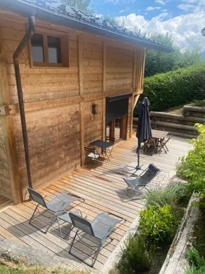 a deck with chairs and an umbrella next to a house at Chalet Charline in Combloux