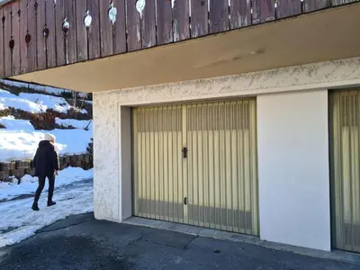 a woman walking past two garage doors in the snow at Appartement Cosy avec Terrasse et Garage in Les Houches