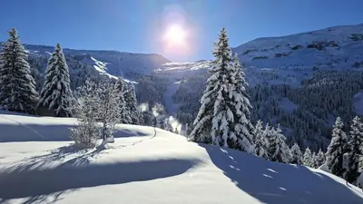 a snow covered mountain with trees and the sun in the background at Résidence Belier - Appartement confortable et spacieux · Au pied des pistes · WIFI gratuit et illimité MAE-8211 in Magland