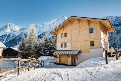 a house in the snow with mountains in the background at Chalet Belle des Neiges - Alpes Travel - Sleeps 9 in Les Houches