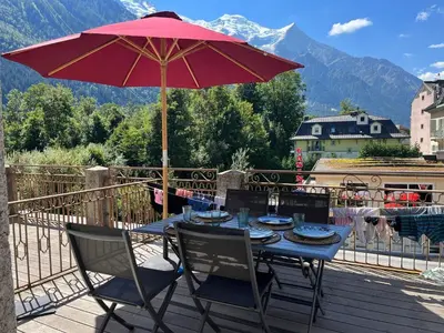 a table and chairs with an umbrella on a balcony at Appart Centre Chamonix Grande Terrasse Mont Blanc in Chamonix-Mont-Blanc