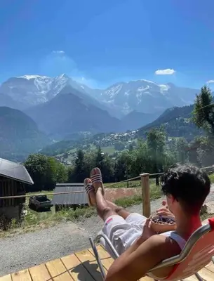 a man is sitting in a chair with his feet up on a mountain at Chalet 3 chambres, 11 personnes près du domaine skiable, parking gratuit, Chez Pépé à Saint-Gervais in Saint-Gervais-les-Bains
