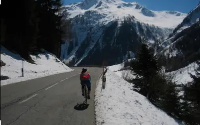 a person riding a bike down a road with a snow covered mountain at Andro in Chamonix-Mont-Blanc