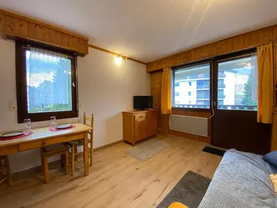 a living room with a table and a desk and two windows at Studio cosy rénové avec balcon et animaux acceptés, centre de Samoëns - FR-1-624-157 in Samoëns