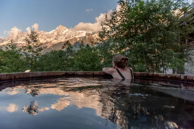 a woman sitting in a swimming pool with mountains in the background at Les Granges d'en Haut - Chamonix Les Houches in Les Houches