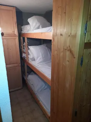 a wooden bunk bed with white sheets and pillows at Le chalet des neiges 3 est au calme situé à 5 mn à pied du centre juste à côté du terrain de foot est composé canapé convertible et 3 lits supperposés parking privé sur place et arrêt navette gratuite à 30 m in Les Carroz d'Araches
