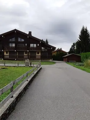 a large wooden building with a fence and a road at Le chalet des neiges 3 est au calme situé à 5 mn à pied du centre juste à côté du terrain de foot est composé canapé convertible et 3 lits supperposés parking privé sur place et arrêt navette gratuite à 30 m in Les Carroz d'Araches