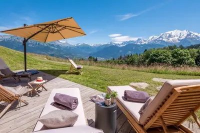a patio with chairs and an umbrella and mountains at Chalet 14 personnes I Luxe I Piscine & Sauna I Salle cinéma I Le Chalet Club in Combloux