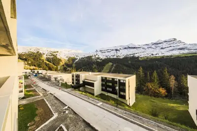 a building with snow covered mountains in the background at Résidence La Petite Ourse - maeva Home - Appartement 4 Pièces 6 Personnes - Sélection MAE-3904 in Arâches-la-Frasse