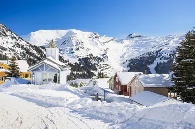 a church covered in snow with mountains in the background at Les Chalets de Flaine Hameau - maeva Home - Chalet 5 Pièces 8 Personnes - Sélection MAE-2135 in Flaine